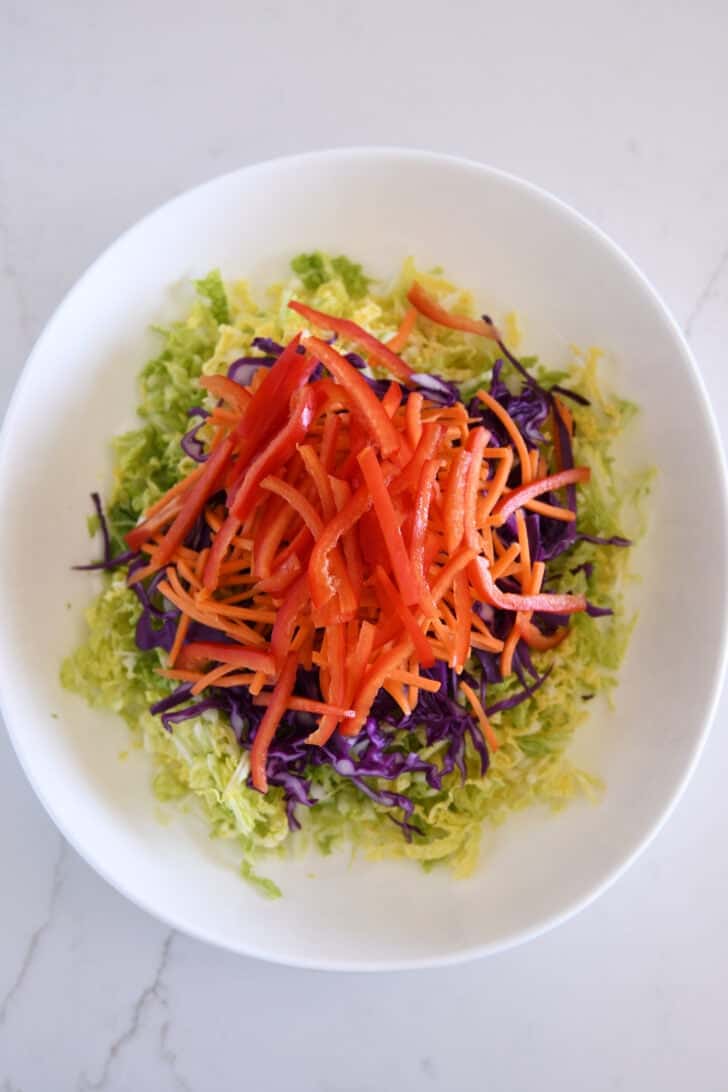 Julienned red peppers in bowl with matchstick carrots, red cabbage and Napa cabbage.