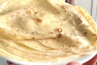 Woman holding plate of cooked crepes.