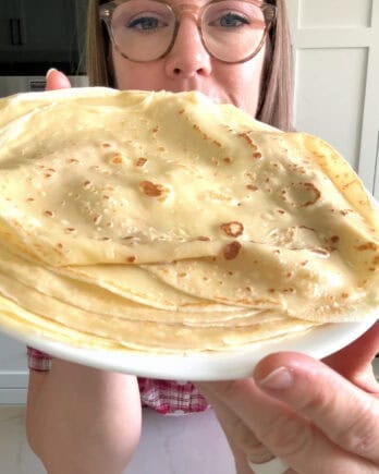 Woman holding plate of cooked crepes.