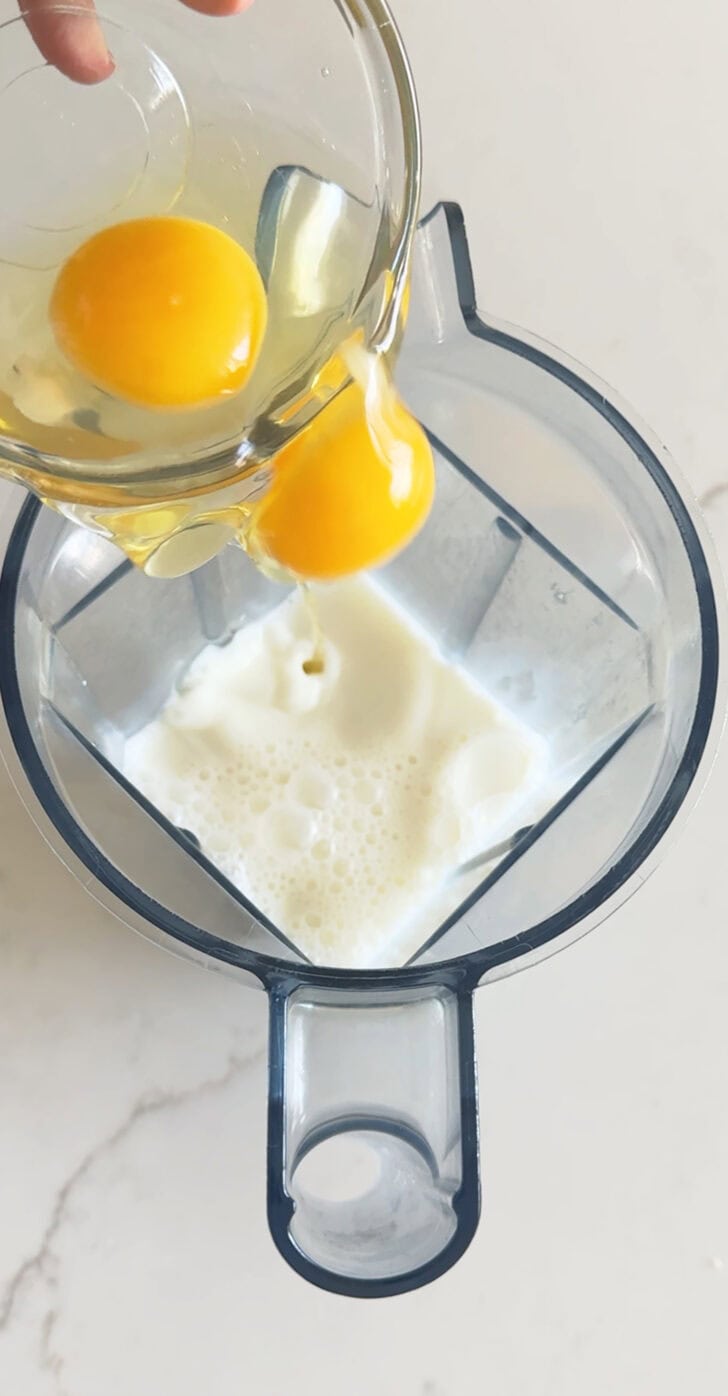 Adding two eggs to blender with milk.