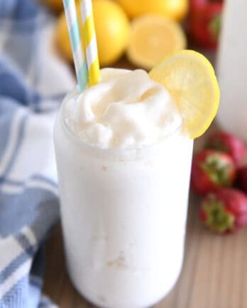 Tall glass filled with frosted lemonade with striped straws and lemon slice for garnish.
