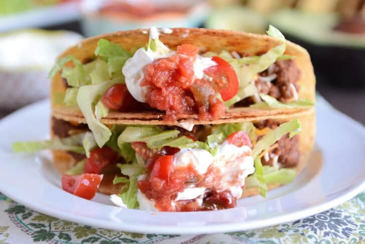 Two ground beef tacos stacked on top of each other on white plate.