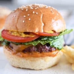 Homemade hamburger bun with juicy burger, lettuce, tomato and mustard.