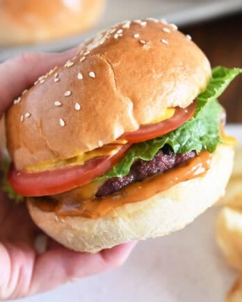 Pressing juicy burger topped with cheese, lettuce, tomato and mustard on homemade bun.