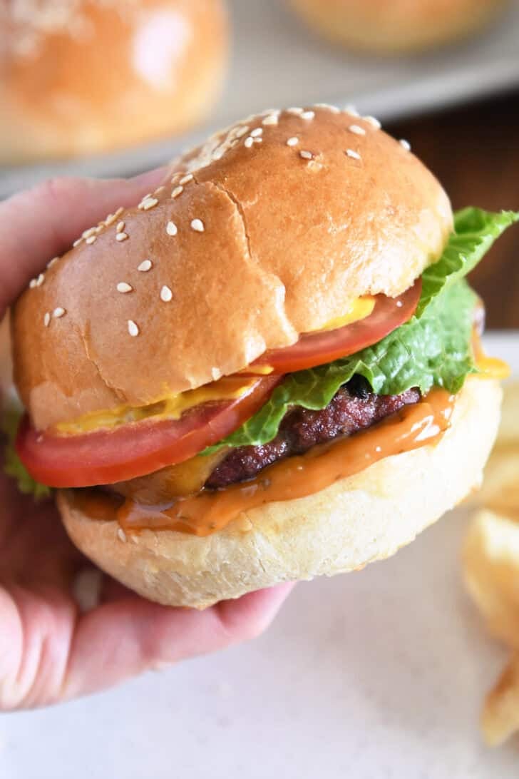 Pressing juicy burger topped with cheese, lettuce, tomato and mustard on homemade bun.