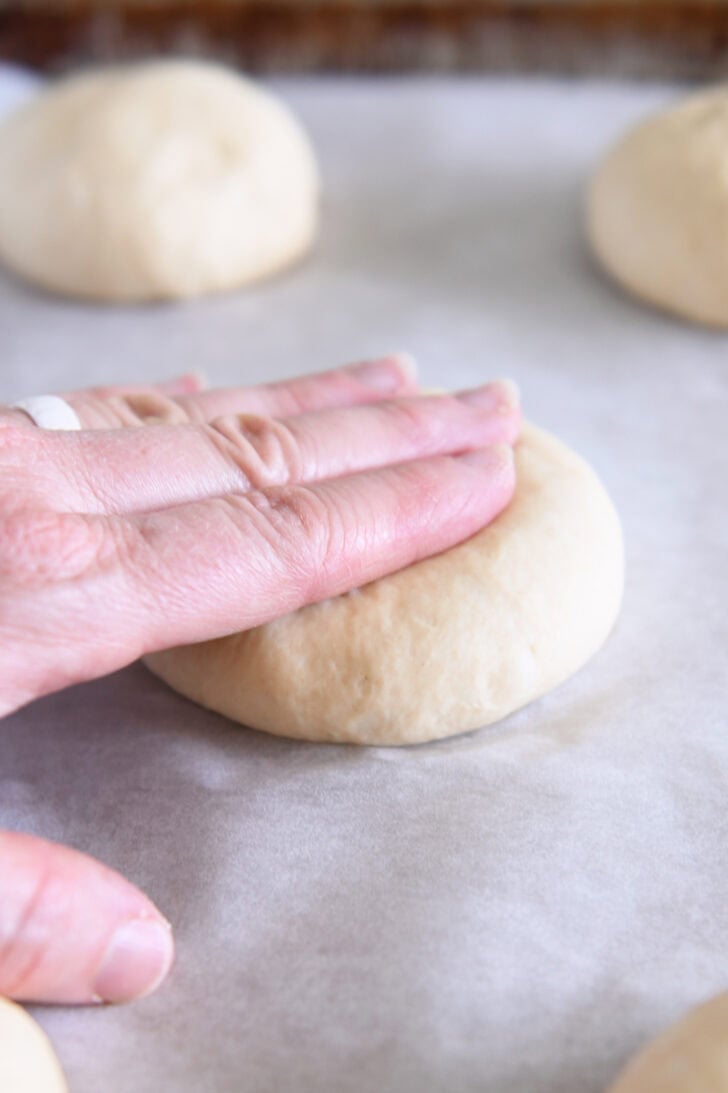 Pressing dough into thick disc shape for homemade hamburger buns.