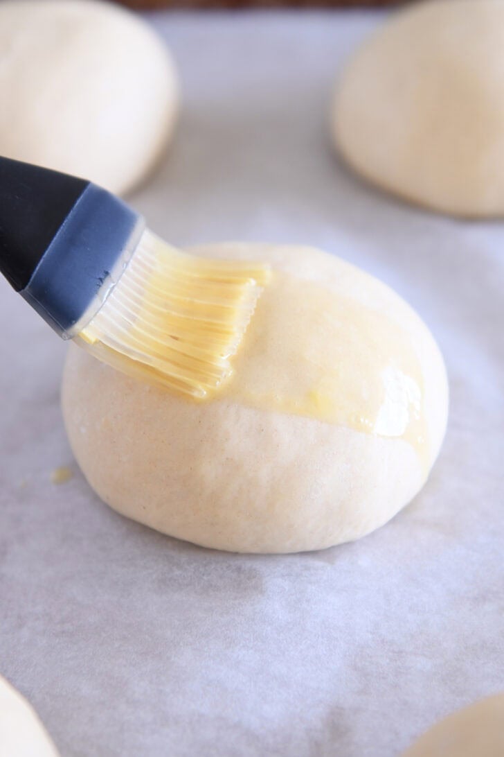 Brushing egg wash on top of hamburger bun dough with pastry brush.