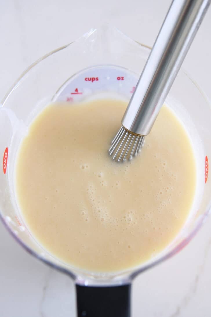 Liquid measuring cup with whisk, pineapple juice, half-and-half and cream of coconut.