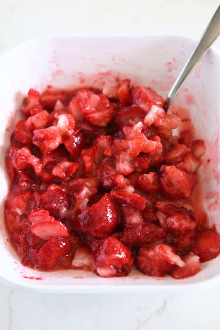 White square bowl with slightly thawed strawberries and sugar.