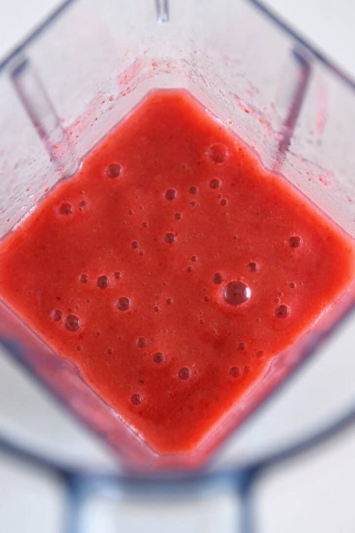 Blender with blended up mixture of slightly frozen strawberries, water and sugar.