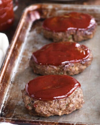 A cookie sheet with three baked mini glazed meatloaves.
