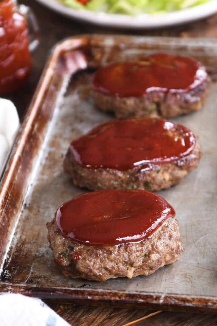 A cookie sheet with three baked mini glazed meatloaves.