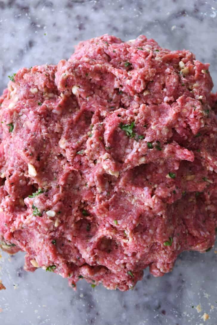 Top down view of a raw meat with spices and bread crumbs in a glass bowl.