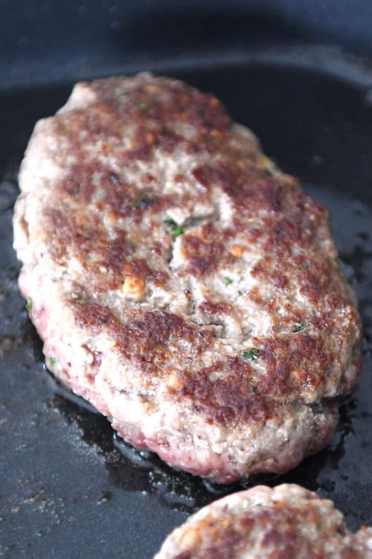 A mini meatloaf getting cooked in oil in a skillet.
