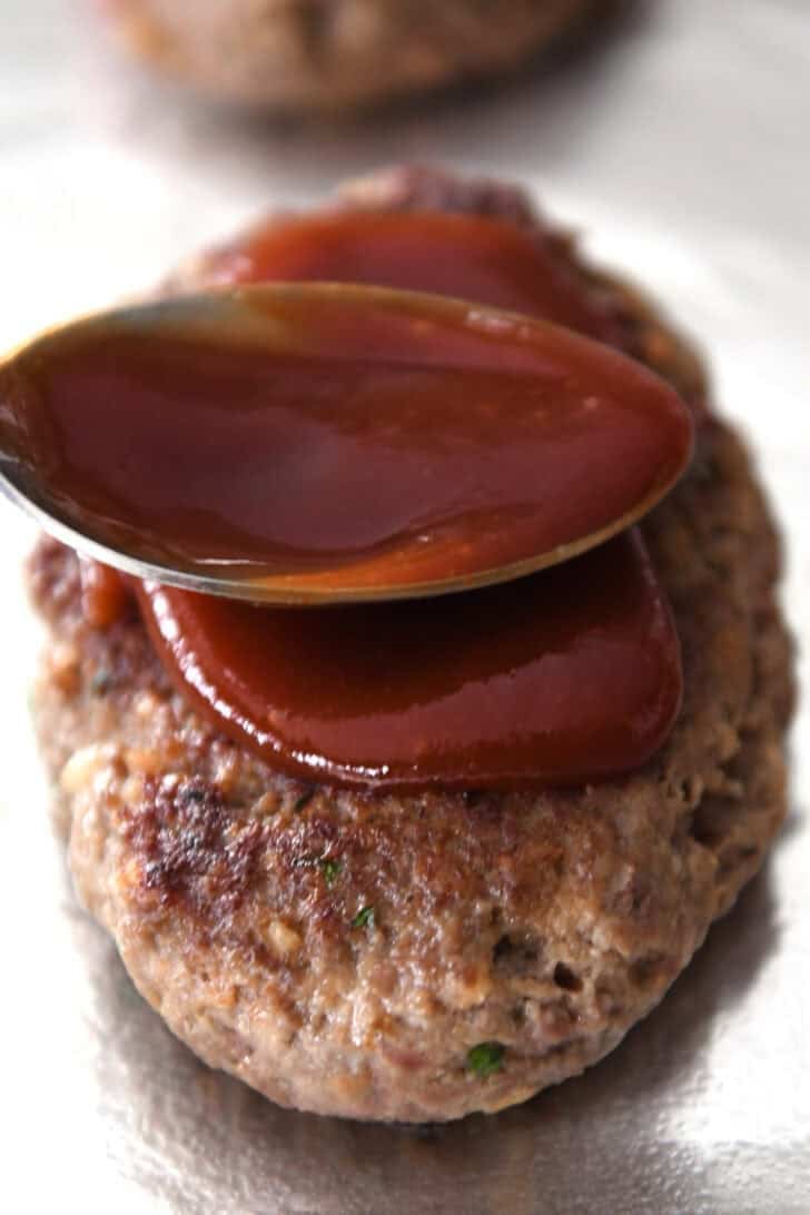 A spoon rubbing a glaze on top of a baked meatloaf.