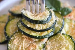 Fork spearing three zucchini rounds on gray plate.