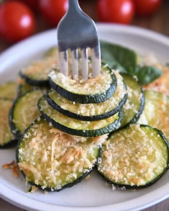 Fork spearing three zucchini rounds on gray plate.