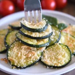Fork spearing three zucchini rounds on gray plate.