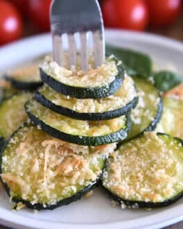 Fork spearing three zucchini rounds on gray plate.