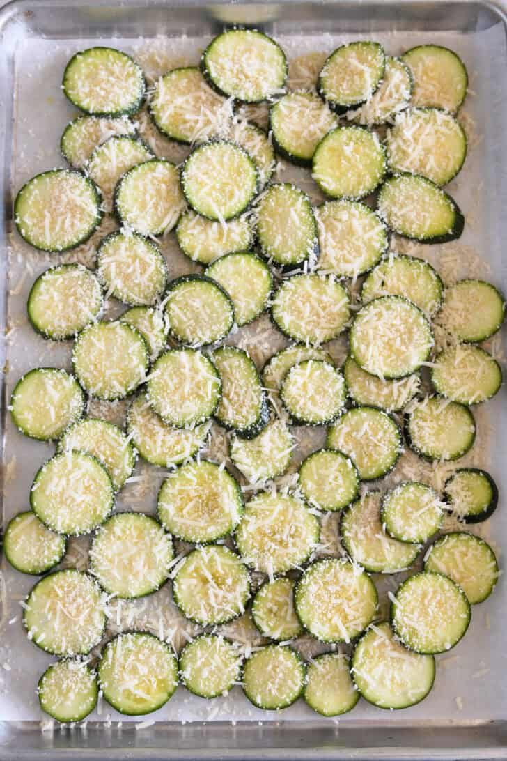Thinly sliced zucchini rounds on half sheet pan topped with panko bread crumbs and Parmesan cheese.