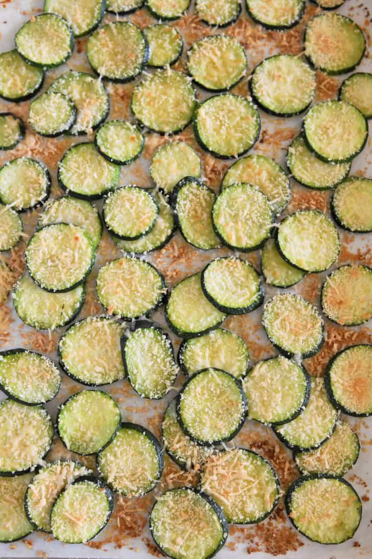 Baked golden zucchini rounds on half sheet pan with bread crumbs and Parmesan cheese.