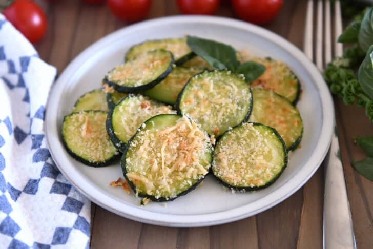 Thinly sliced baked zucchini rounds on plate topped with panko bread crumbs and Parmesan cheese.