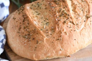 Top down view of a golden brown loaf of rosemary bread on a cutting board.