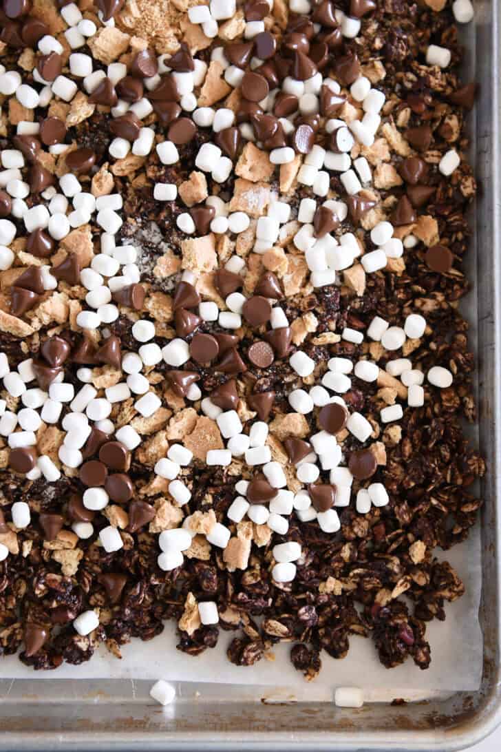 Baked chocolate granola on sheet pan topped with graham cracker pieces, mini marshmallows and melty chocolate chips.
