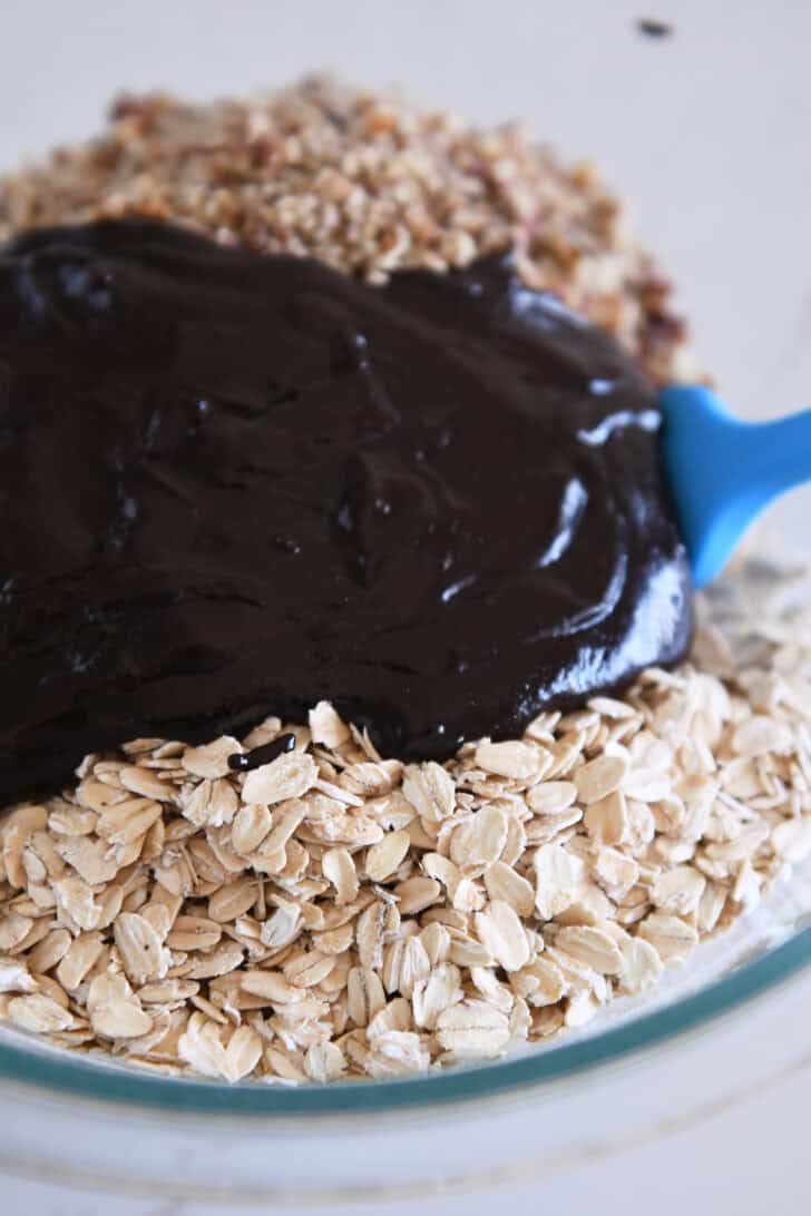 Chocolate syrup poured over oats and pecans in glass bowl.