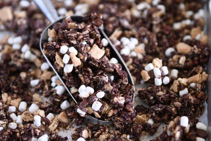 Metal scoop filled with chocolate granola, graham crackers, and mini marshmallows.