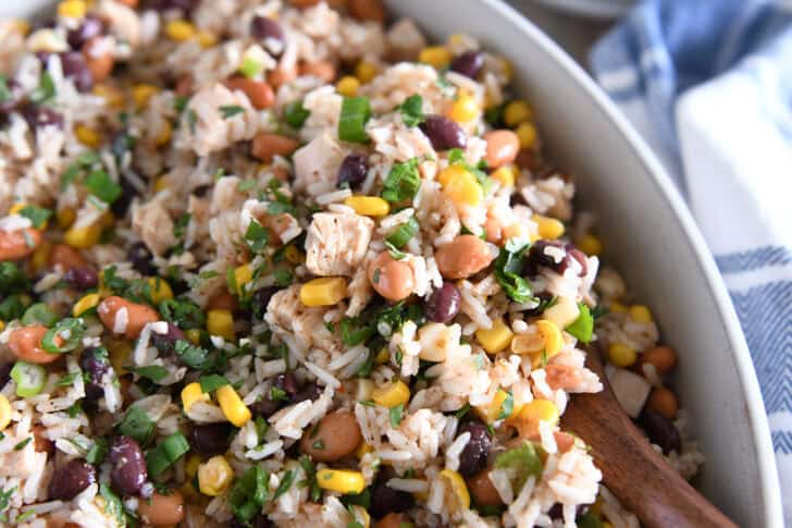 Top down view of a white dish with a rice, bean, and chicken salad topped with chopped cilantro.