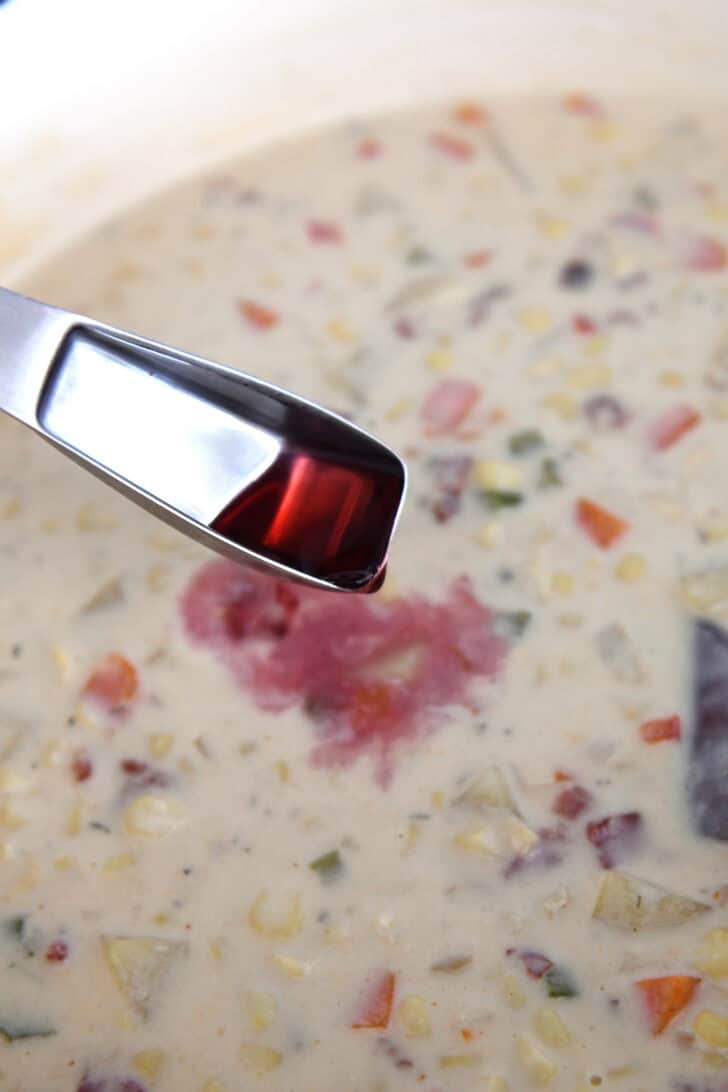 Pouring in tablespoon of red wine vinegar to pot of corn chowder.