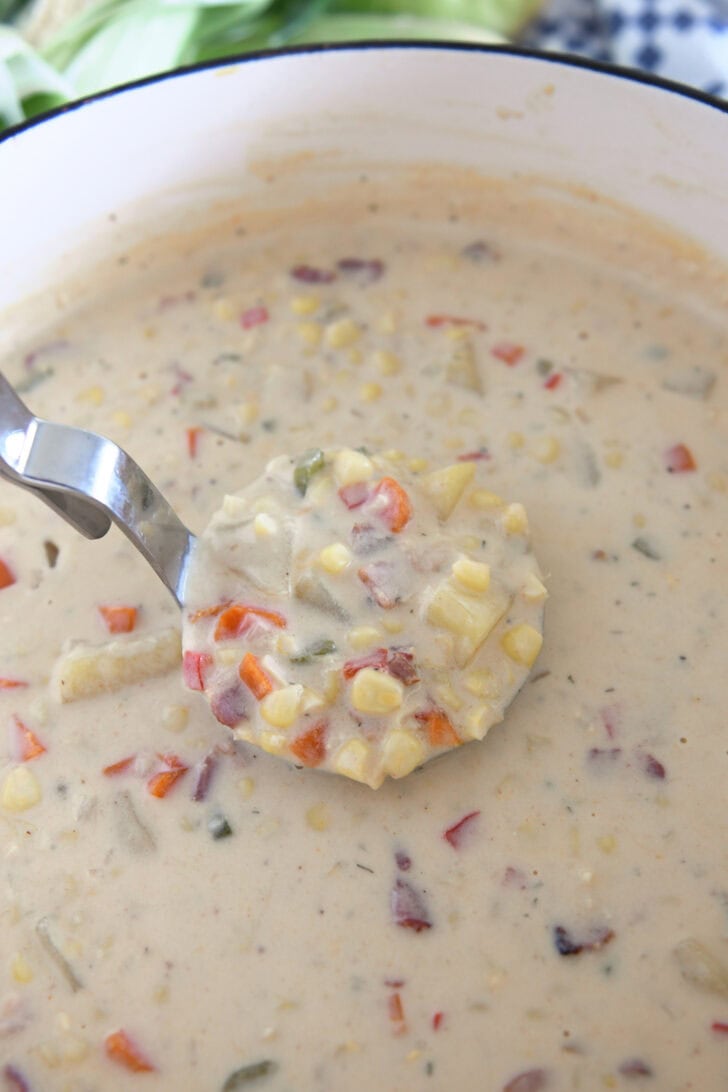 Ladle in pot scooping up thick and creamy corn chowder with carrots, bacon and potatoes.