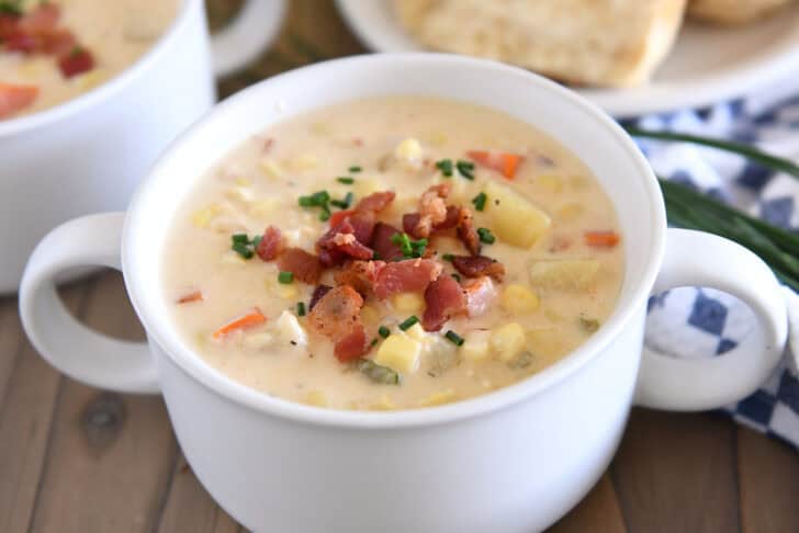 White bowl with handles filled with thick and creamy corn chowder topped with bacon pieces.