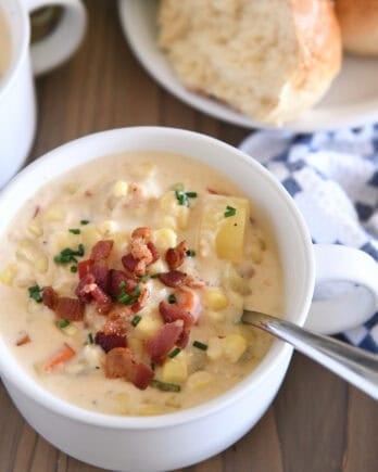White bowl with spoon scooping up chowder with fresh corn, bacon, potatoes and carrots.