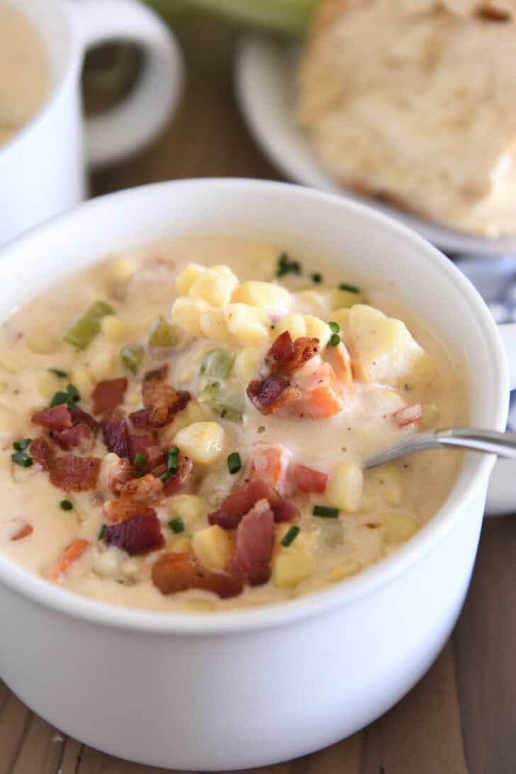 White bowl with spoon scooping up chowder with fresh corn, bacon, potatoes and carrots.