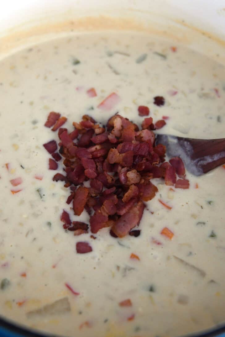 Cooked bacon pieces in pot with thick and creamy corn chowder.