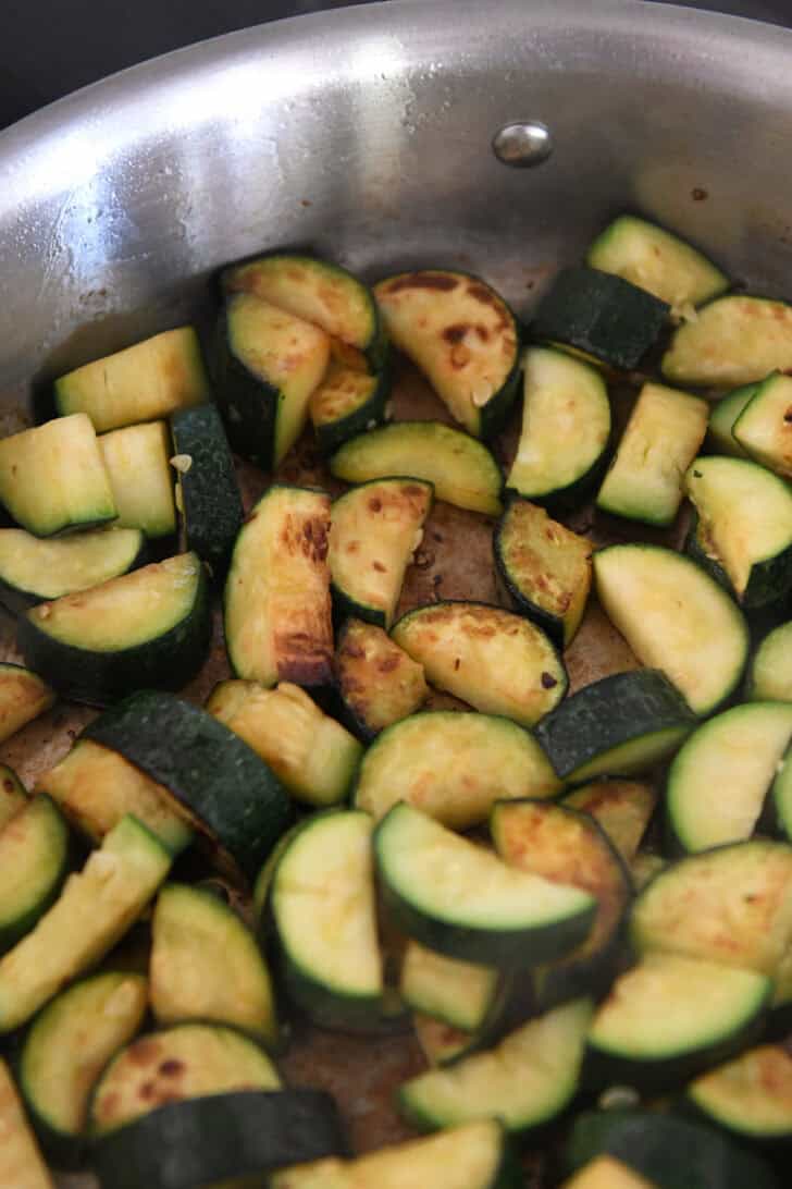 Stainless skillet with browned zucchini pieces.
