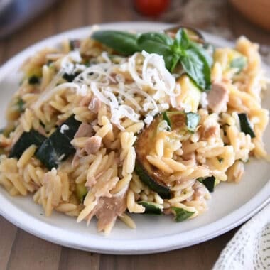 Orzo with tuna, zucchini, and Parmesan with fresh basil as a garnish on gray plate.