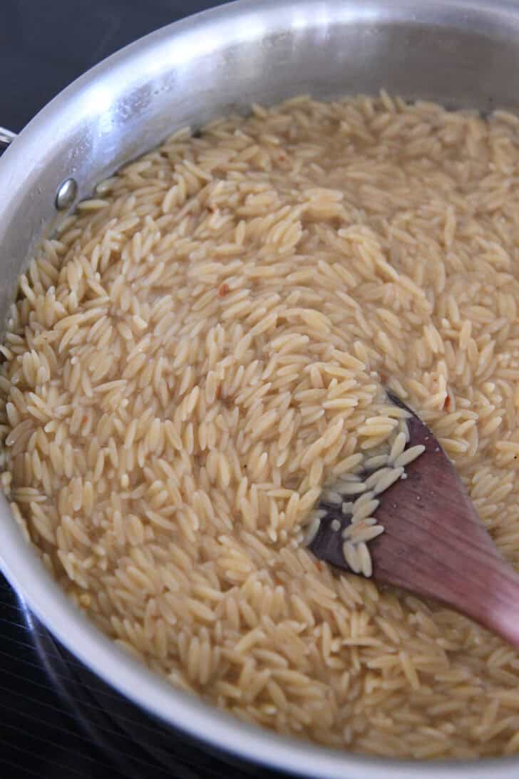 Stainless skillet with orzo cooking in chicken broth.