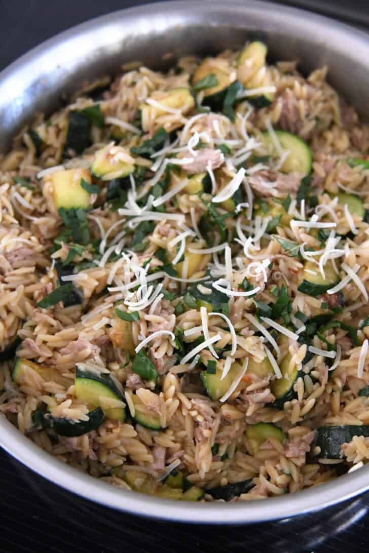 Stainless skillet with cooked orzo, tuna, zucchini, fresh basil and parmesan cheese.
