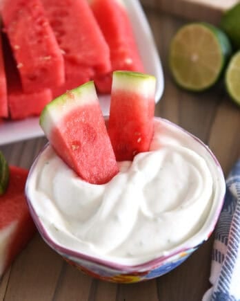 Two watermelon sticks dipped in Greek yogurt creamy watermelon dip.
