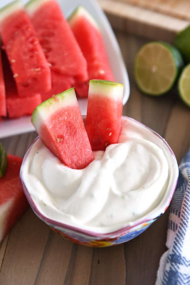 Two watermelon sticks dipped in Greek yogurt creamy watermelon dip.