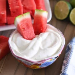 Two watermelon sticks dipped in Greek yogurt creamy watermelon dip.