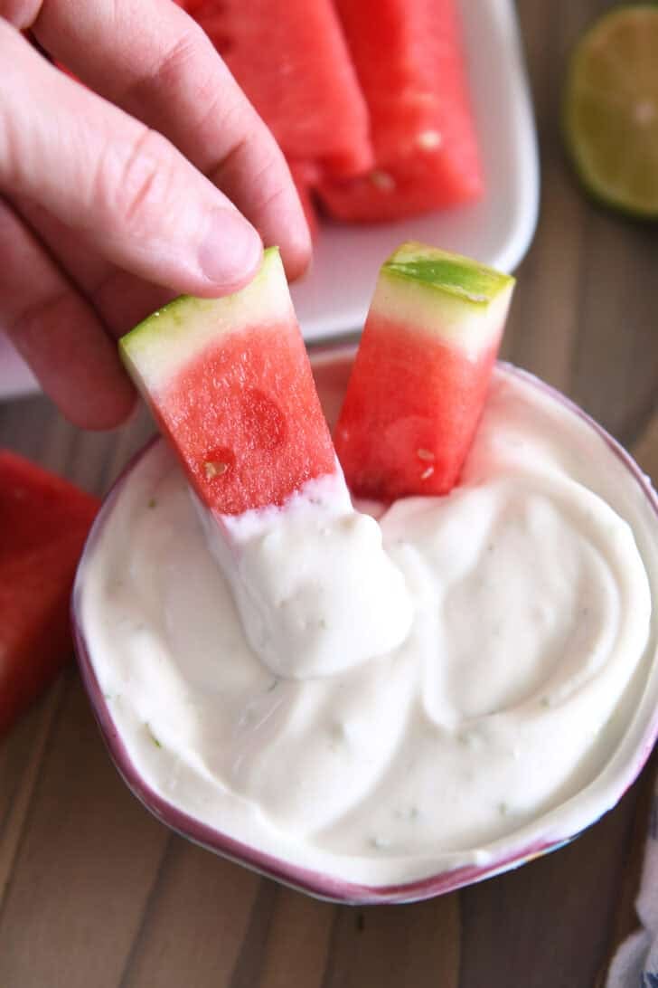 Two watermelon sticks dipped in Greek yogurt creamy watermelon dip.