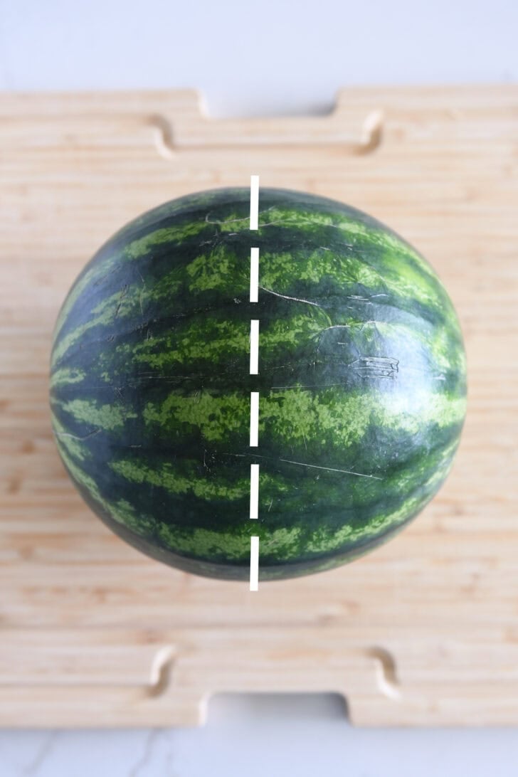 Watermelon on wood cutting board with strip showing where to cut it in half.