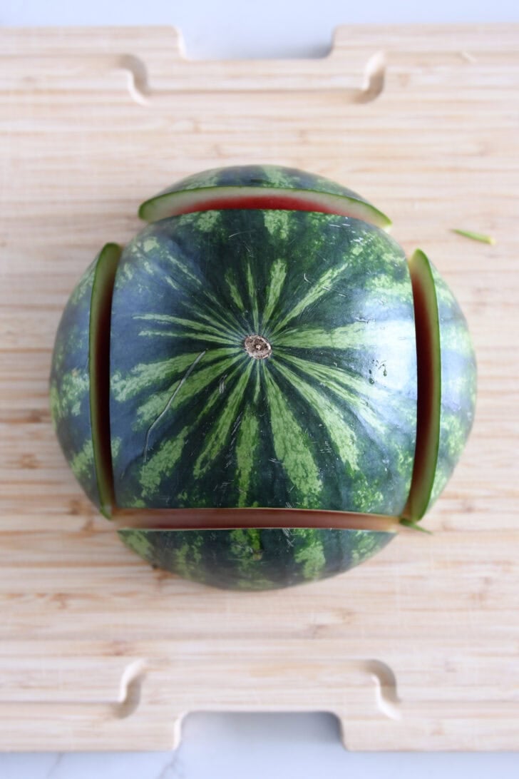 One half of a watermelon turned cut-side down on a wood cutting board with all four rounded edges cut off.