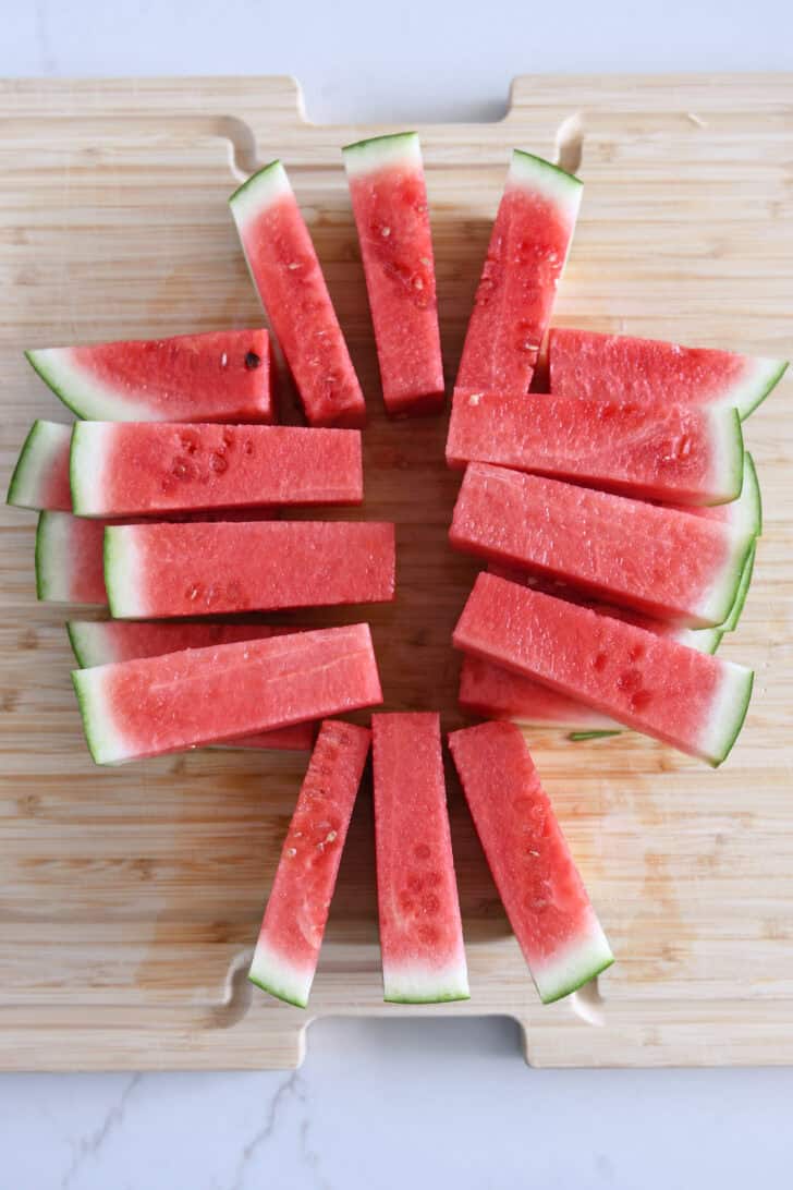 Watermelon cut into sticks on wood cutting board.