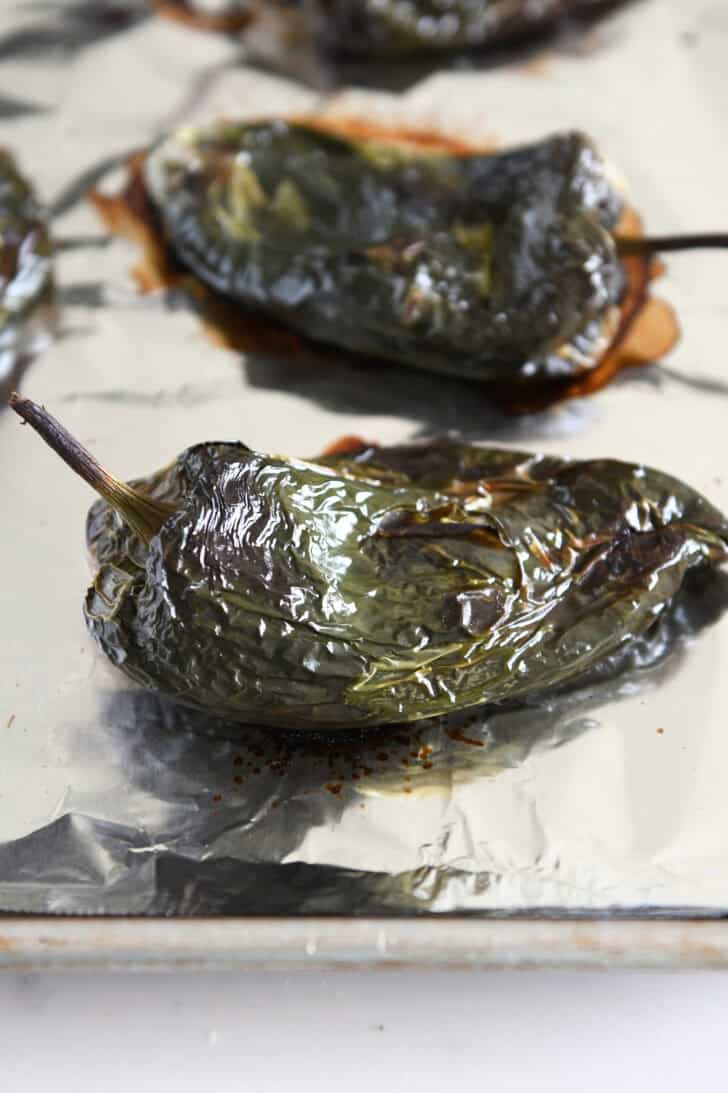 Roasted green chile peppers on a tinfoil-lined cookie sheet.