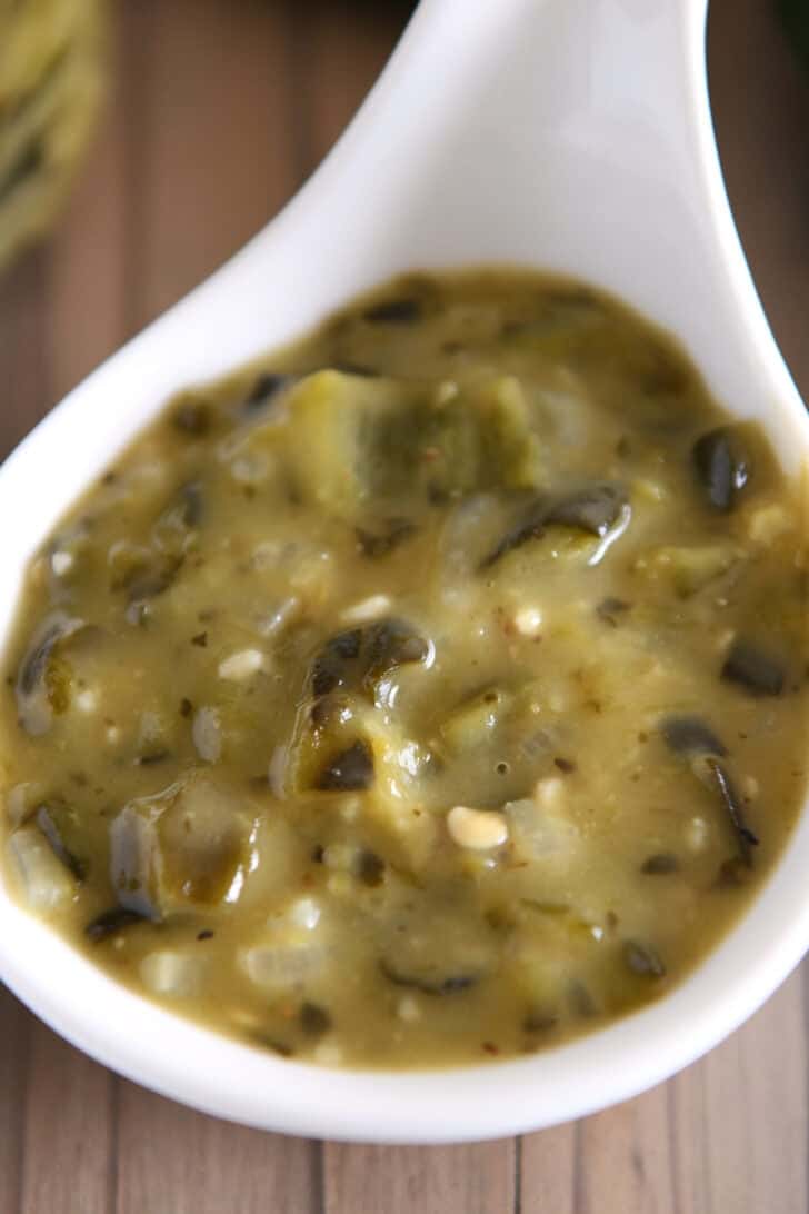 Top down view of a white ladle filled with green enchilada sauce.